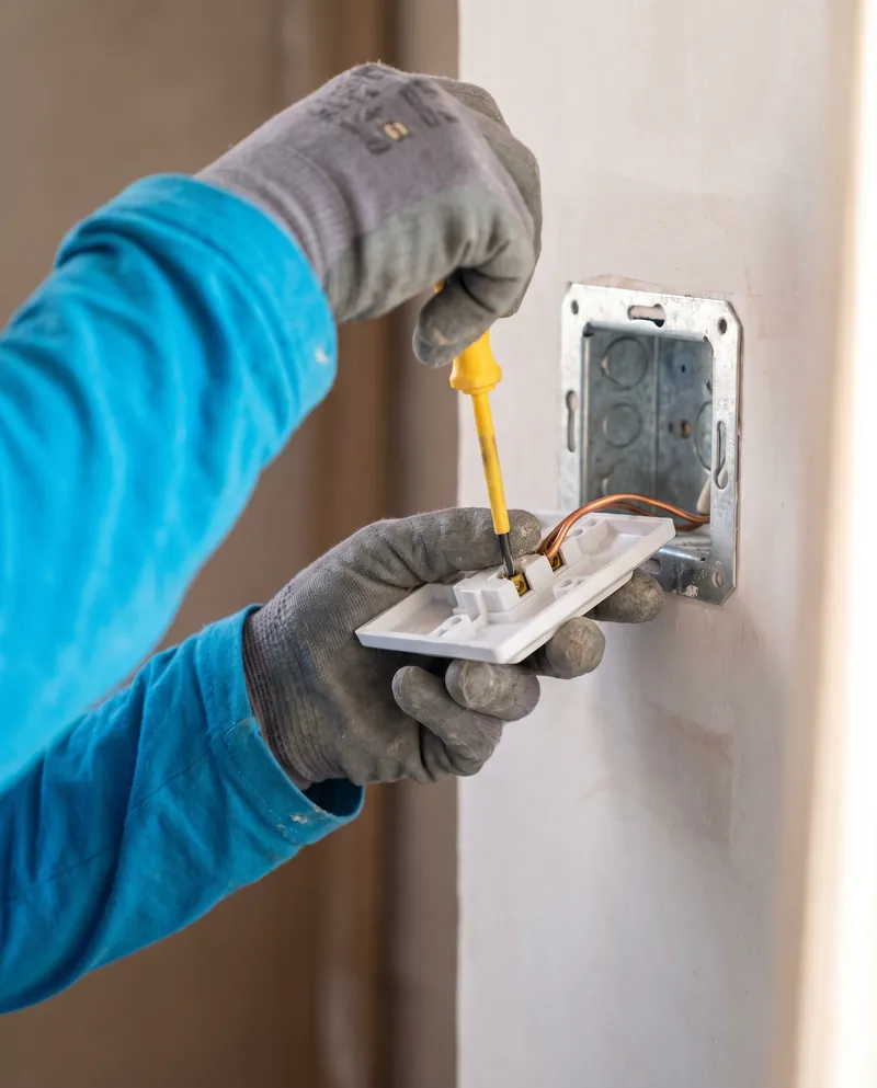 Hands in work gloves and blue sleeves wiring a new socket