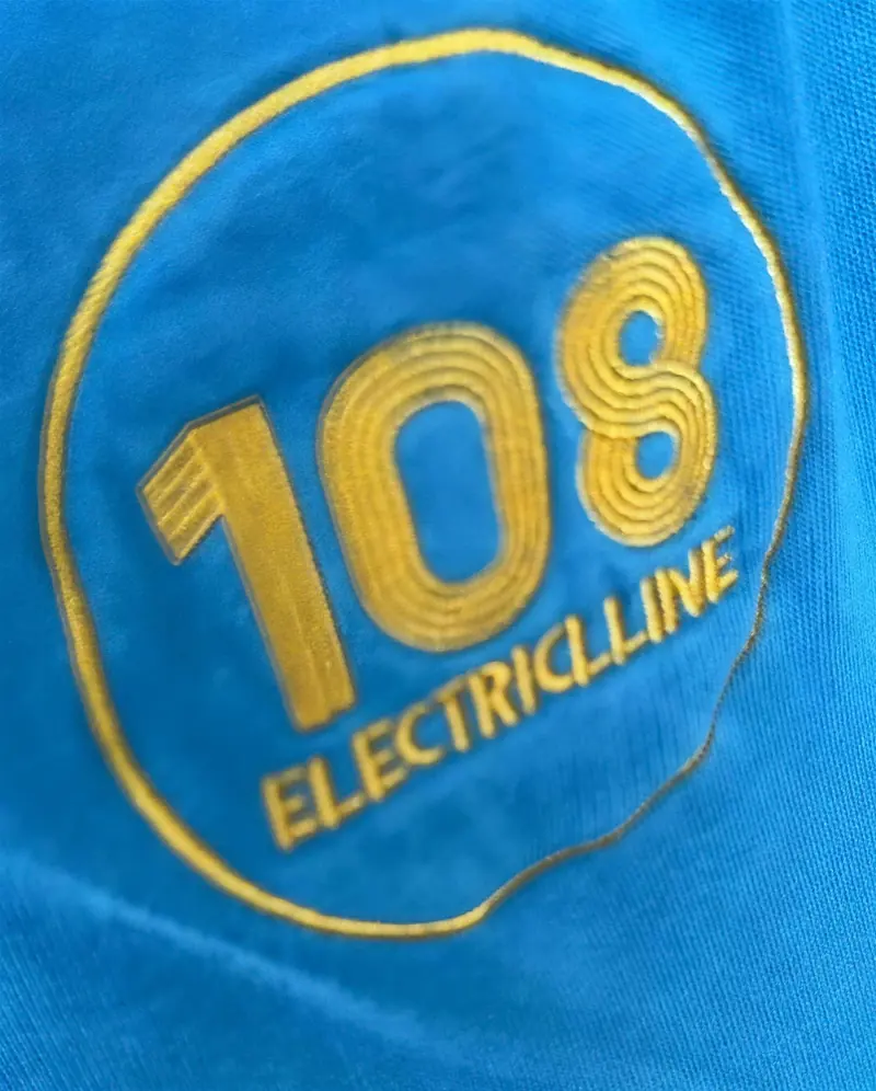 The gold 108 Electriclline badge embroidered on an azure work shirt
